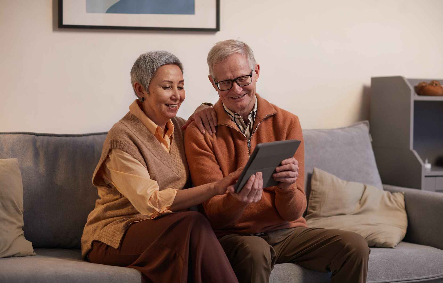 man and woman sitting on sofa while looking at a tablet computer