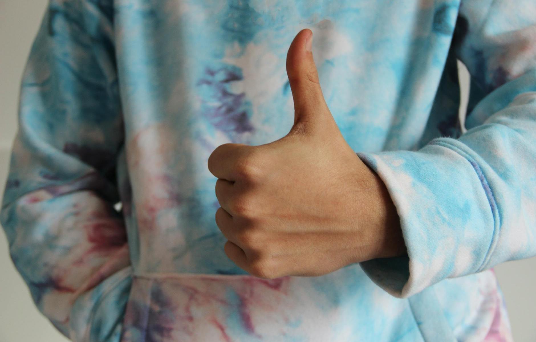 a person in tie dye sweater doing thumbs up